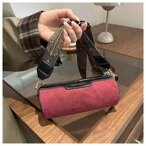 Close-up of matte wine red cylinder bag with ethnic woven strap and golden branding