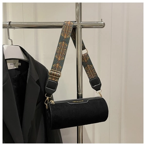 Detail of black suede cylinder bag featuring a vintage patterned wide jacquard strap