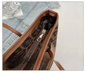 Detail von goldenem Metallreißverschluss und braunem Lederbesatz auf Leopard-Tote