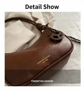 Detailansicht der braunen Leder-Hobo-Tasche mit Goldlogo und dunklem Anhänger