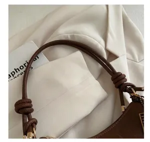 Detail der braunen Ledertasche mit Knotengriff und goldener Hardware auf weißem Blazer