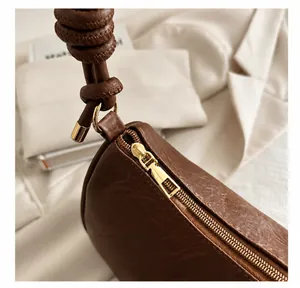 Dettaglio della borsa sottobraccio in pelle marrone con texture litchi e zip dorata