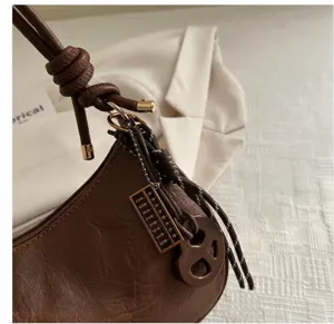 Details einer kaffeebraunen Ledertasche mit Knotengurt und goldenem Abakus-Anhänger