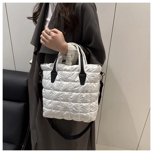 Detail of white quilted tote bag with black strap and silver metal buckle on grey coat