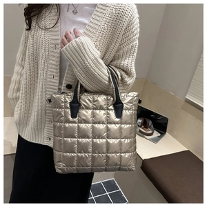 Detail of champagne gold puffer tote bag featuring square quilting and black straps
