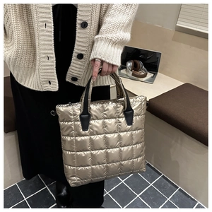Detail of champagne gold quilted tote bag featuring metallic gloss and black handles