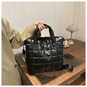 Detail of black quilted puffer tote bag with sturdy handles and adjustable woven strap