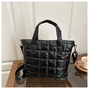 Detail of black quilted puffer tote bag with detachable shoulder strap on table