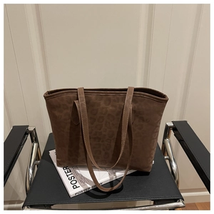 Sac fourre-tout léopard en daim posé sur un magazine avec une chaise noire chic