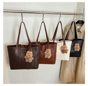 Detail of woven tote bags in brown, white, and black with cute bear charms on metal hanger
