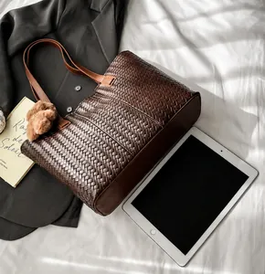Detail of dark brown woven leather tote bag with pompom charm and textured surface
