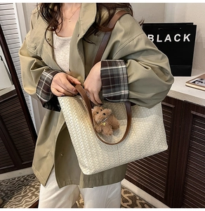 Detail of woven cream tote bag with brown leather handles and teddy bear pendant accessory