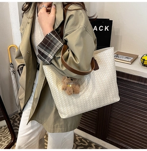 Detail of white woven tote bag with brown leather straps and a plush bear charm