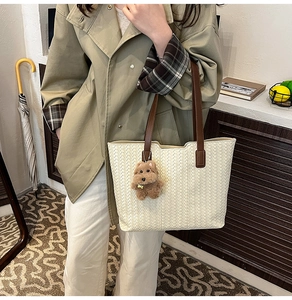 Detail of woven cream leather tote bag with brown handles and a cute dog plush charm