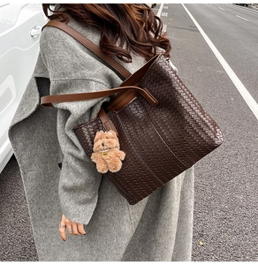 Detail of dark brown woven leather tote bag with a cute plush bear charm on a shoulder strap