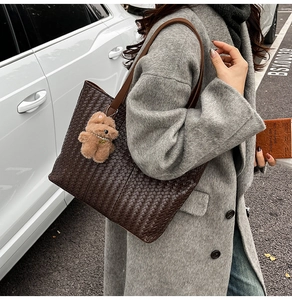 Detail of dark brown woven leather tote bag with a plush bear charm and pearl necklace