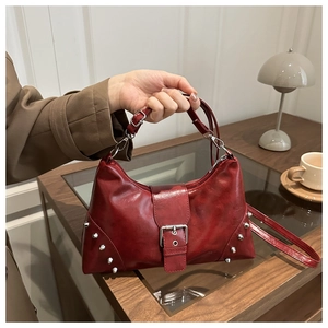 Detail of red vintage tote bag with silver rivets and buckle on dark wooden desk