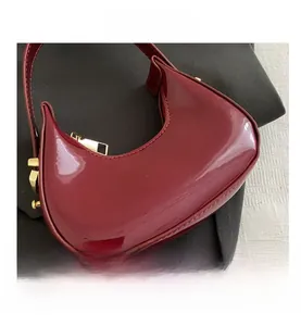 Macro shot of glossy burgundy crescent bag with polished gold metal hardware