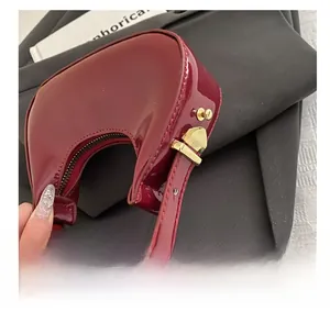 Detailed close-up of wine red patent leather crescent bag with gold metal hardware buckle