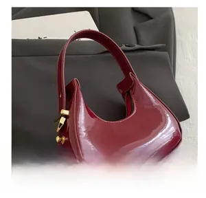 Detail showing glossy burgundy patent leather crescent bag with elegant gold hardware