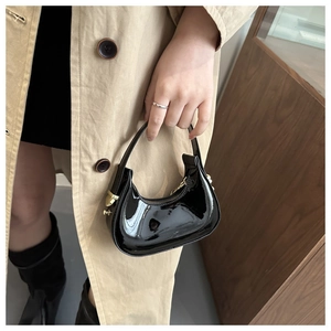 Detail of glossy black crescent bag with gold hardware worn with a beige trench coat