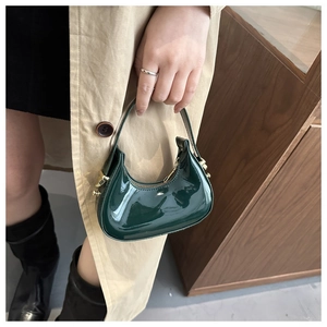 Close-up of a dark green crescent handbag in shiny patent leather with gold hardware