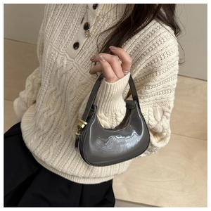 Detail view of grey patent leather crescent bag with gold zipper and polished mirror finish