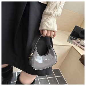 Detail of grey patent leather crescent bag with golden hardware in an urban setting