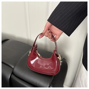 Close-up of burgundy crescent bag in glossy patent leather with gold-tone hardware detail
