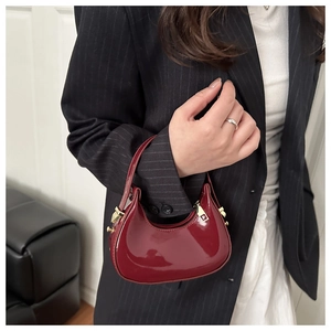 Detail of burgundy patent leather crescent bag with gold hardware and mirror finish