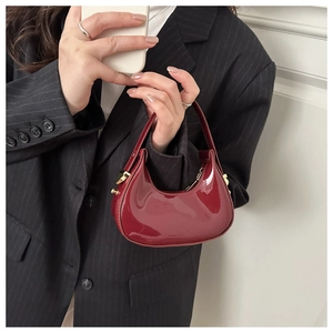 Macro detail of red patent leather crescent bag with glossy finish and gold metal hardware