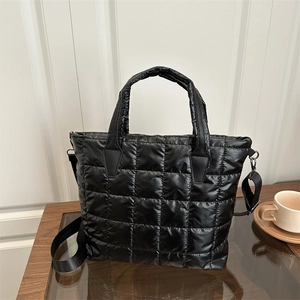 Quilted black nylon tote bag with shoulder strap on a wooden table in a home setting