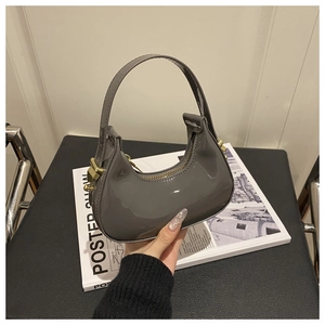 Detail of grey patent leather crescent bag with gold hardware on a magazine