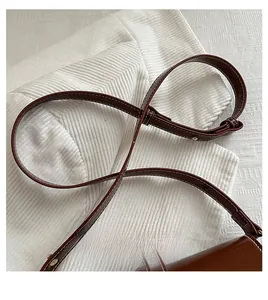 Detail of dark brown leather shoulder strap with white contrast stitching and gold buckle
