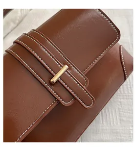Macro view of brown leather shoulder bag with white contrast stitching and gold metal buckle