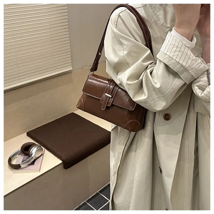 Brown vintage underarm bag with white contrast stitching and gold buckle worn with a trench coat