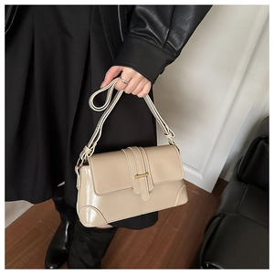 Detailed view of beige leather shoulder bag featuring gold buckle and patch details