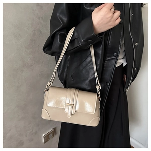 Detail of glossy beige shoulder bag featuring a sleek metal buckle and vertical strap
