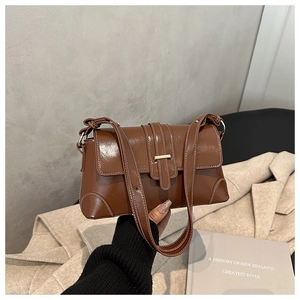 Detailed view of brown leather shoulder bag with gold clasp and white contrast stitching