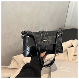 Close-up of black glossy shoulder bag with white contrast stitching and gold buckle