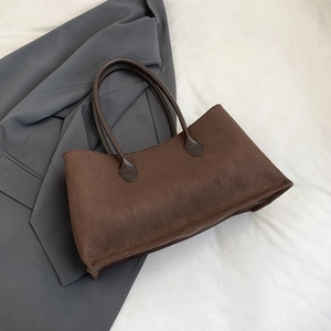 Gros plan d'un sac cabas en daim marron foncé avec poignées renforcées sur veste grise