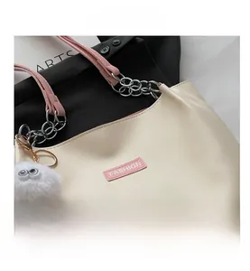 Detail view of cream PU tote bag with pink metal chain strap and plush keychain charm