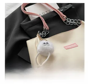 Close-up of a white plush monster charm with big eyes on a beige tote bag