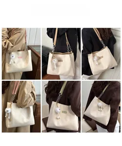 Detail view of ivory tote bag with metal chain strap and cute plush charm on a model