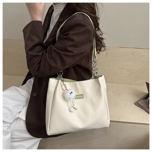 Detail of cream white tote bag with green straps and soft plush pendant accessory