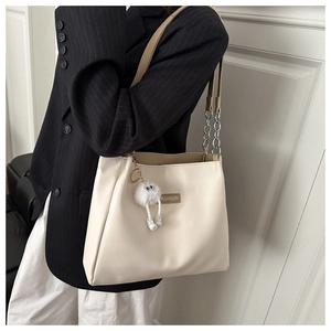 Detail of off-white tote bag with metal chain strap and cute white plush toy accessory