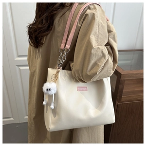 Detail of cream tote bag featuring pink strap, silver chain, and cute plush charm pendant