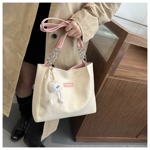 Detail of cream white tote bag with pink straps and plush charm on metal chain