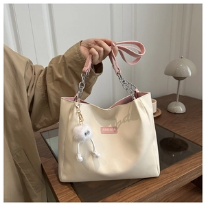 Detail of cream tote bag with pink straps, chain handle and fluffy monster charm