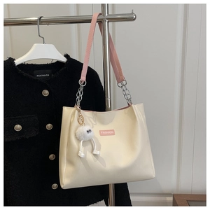 Detail of cream white tote bag with pink straps and a cute plush monster charm
